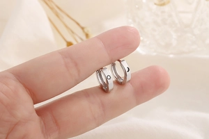 Close-up of minimalist silver sun and moon hoop earrings shown on a finger for scale