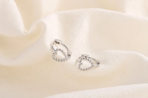 Gros plan de boucles d'oreilles cœur en argent avec zircons sur tissu en lin beige