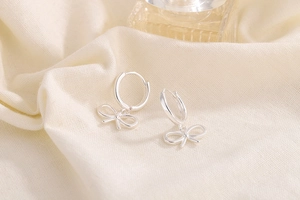 Elegant silver bow pendant earrings on soft beige linen fabric with warm lighting