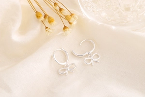 Detail view of silver bow-shaped drop earrings with a polished finish on beige fabric