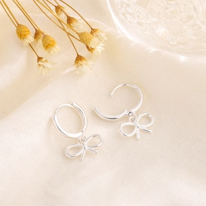 Elegant silver bow pendant hoop earrings on minimalist cream linen fabric background