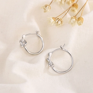 Close-up of silver knot hoop earrings on beige fabric with dried floral accents