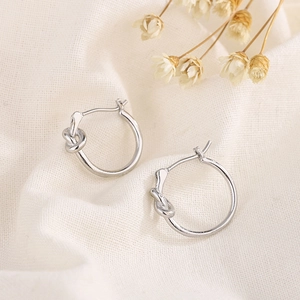 Minimalist silver knot hoop earrings on soft linen background with dried flowers