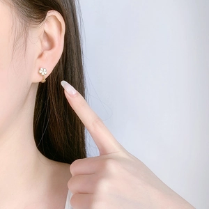Detailed view of model wearing small gold hoop earrings with white enamel five-petal flowers