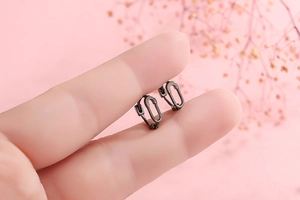 Macro detail of minimalist black safety pin hoop earrings held between fingertips