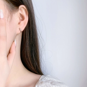 Close-up of minimalist S925 sterling silver cross earring worn by a model in a studio