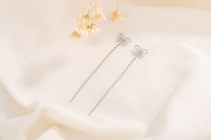 Gros plan de boucles d'oreilles nœuds à pampilles en argent S925 sur lin avec fleurs séchées