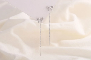 Détail de boucles d'oreilles nœud S925 argent avec chaîne à pompons sur tissu blanc