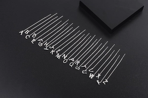Macro display of 26 silver alphabet initial necklaces arranged on black textured background