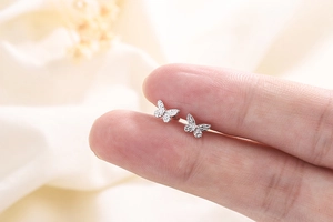 Macro detail of silver butterfly screw back earrings held on a fingertip for size