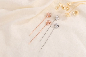 Close-up of four-leaf clover ear threads with sparkling zircons on soft linen fabric