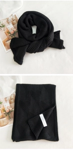 Detail of chunky knit black scarf with heart patterns and woven brand care label