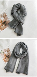 Close-up of thick grey knitted scarf with textured heart pattern on soft fabric