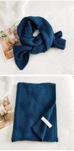 Detail of navy blue knitted scarf with heart patterns and woven label on white fabric
