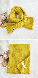 Detailed view of yellow knitted scarf with 3D heart pattern and woven care label