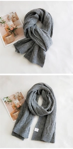 Detailed close-up of dark grey chunky cable knit scarf with soft texture and white label
