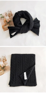 Detail of black cable knit scarf showing premium thick texture and woven labels