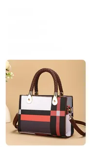 Detail of color-block tote bag with woven handles and golden metal buckles on warm backdrop