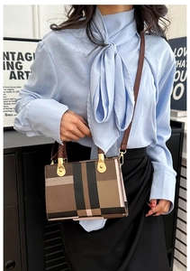 Detail of checkered canvas crossbody bag with gold metal handle and leather strap