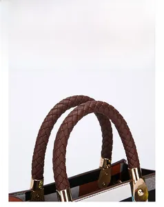 Close-up of woven leather handle and gold hardware on a textured fabric handbag
