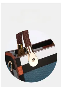 Detail of woven tote bag with striped pattern, brown braided handle and gold hardware