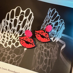 Detail of red resin lip earrings with pink beaded studs on an abstract background
