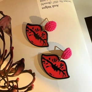 Detail of red lip earrings and magenta beads on white magazine with dried flowers