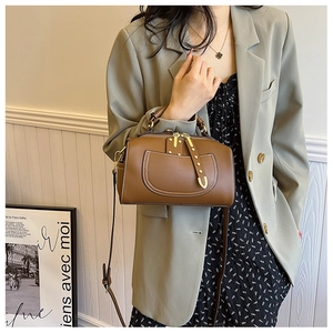 Sac Boston en cuir marron avec surpiqûres blanches et rivets porté par un mannequin