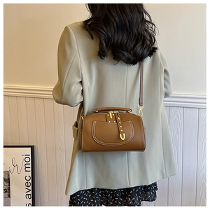 Détail d'un sac docteur en cuir marron avec garnitures dorées et coutures blanches sur blazer