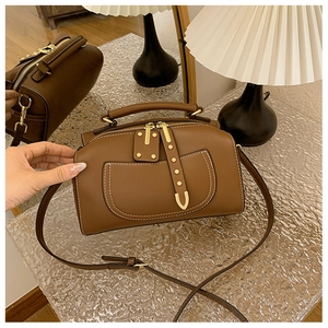 Détail du sac Boston en cuir marron avec rivets dorés et bandoulière réglable