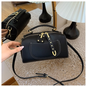Détail du sac Boston noir avec surpiqûres blanches, rivets dorés et reflet miroir
