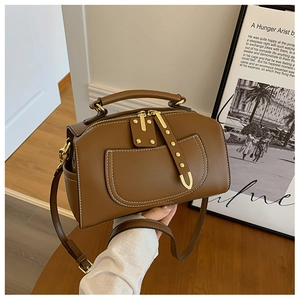 Gros plan d'un sac en cuir marron avec surpiqûres blanches et détails métalliques dorés