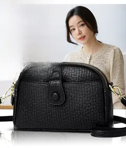 Detail of a black pebbled leather crossbody bag with gold hardware worn by a model