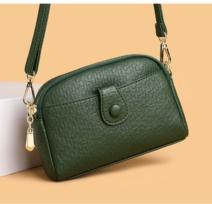 Detail of dark green lychee grain leather crossbody bag with golden hardware and clasp