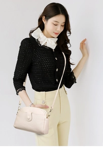Detail view of cream leather shell bag with adjustable strap and golden metal hardware