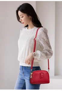 Close-up of a stylish red textured leather crossbody bag worn by a model in casual attire