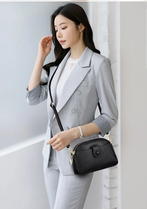 Chic black shell crossbody bag with embossed texture and gold hardware on grey suit