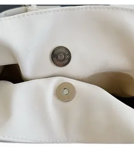 Detail view of the silver metal magnetic buckle and textured leather on a white handbag