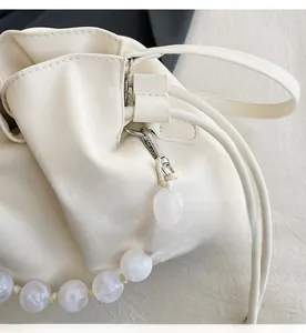 Detail of cream drawstring bucket bag showing silver hardware and decorative pearl chain