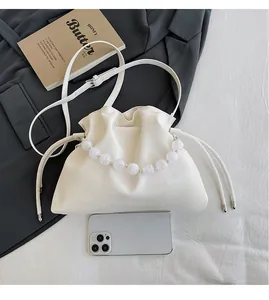 Detail view of cream pleated bucket bag with beaded handle showing smartphone size comparison