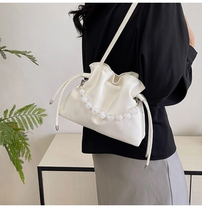 Detail of white pleated cloud bag featuring marble beads handle and drawstring closure