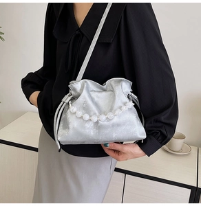 Detail of silver pleated bucket bag featuring large white decorative beads and thin strap