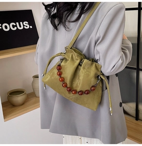 Detail of green suede bucket bag featuring amber beaded handle and drawstring closure