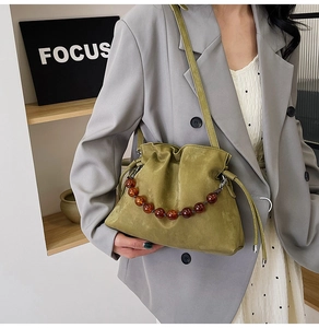 Detail of moss green pleated bucket bag featuring decorative amber beaded handle