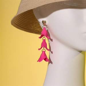 Vue détaillée des boucles d'oreilles pétales magenta et cœur doré sur un modèle avec chapeau