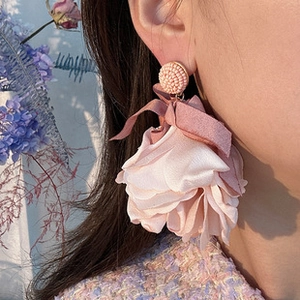 Detail view of large pink fabric flower earrings with bow and beadwork on a model