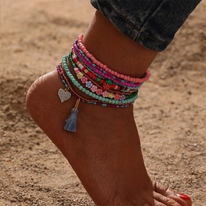 Detail of bohemian layered anklets with heart charm, colorful beads and blue tassel on sand
