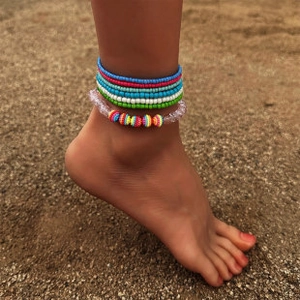 Detail of multi-layered bohemian colorful beaded anklet set worn on a sandy beach