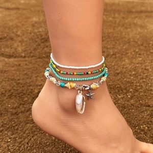 Detail of bohemian layered anklet set with shell and starfish charms on a beach
