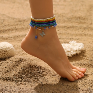 Nahaufnahme bunter Perlen-Fußkettchen mit Schmetterlingsanhänger auf feinem Sandstrand